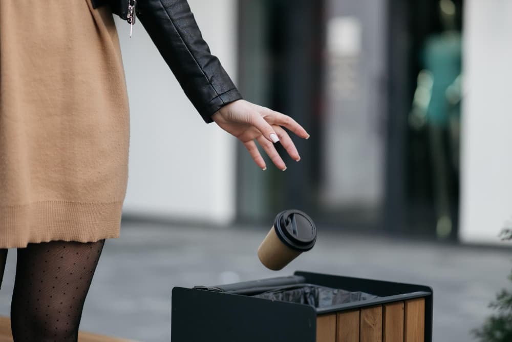 woman throwing away a coffee cup into a trash can on the street